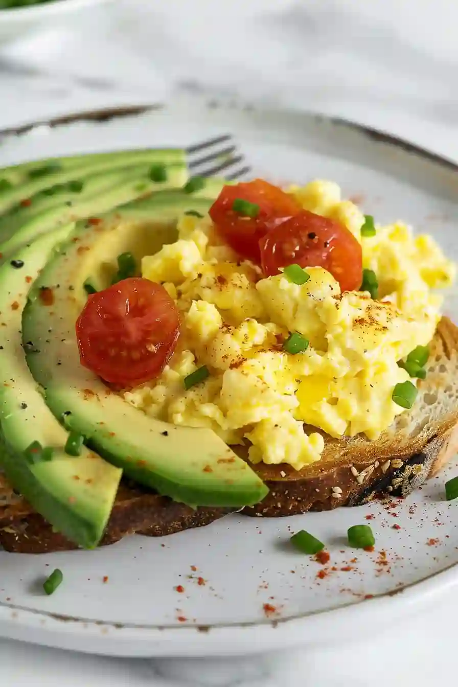 Avocado Toast with Scrambled Eggs Plate eggs over avocado toast plated with tomatoes and green onions