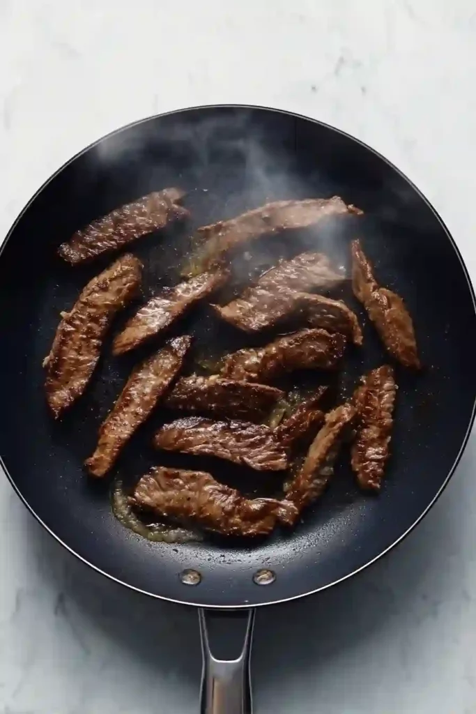 Beef strips browning in a pan on stovetop close-up