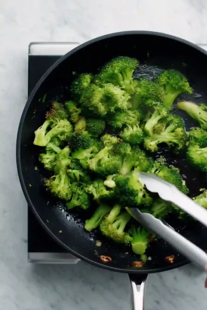 Broccoli florets cooking in a pan with tongs close-up