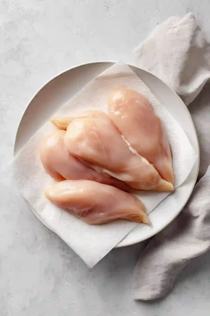 raw chicken breasts on white plate with paper towel removing moisture