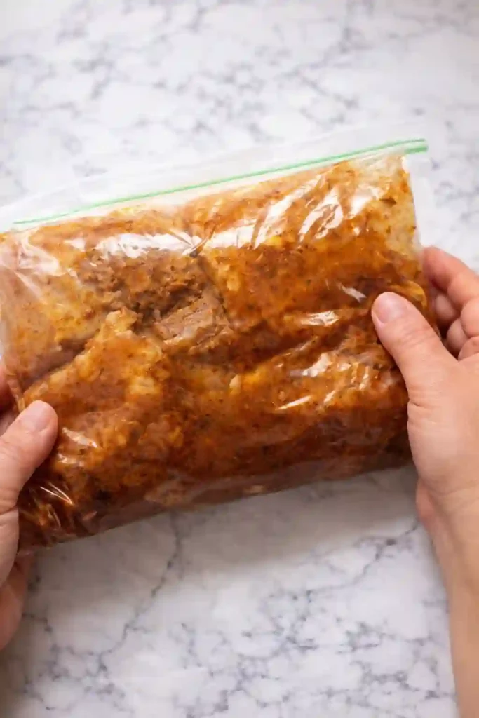 Easy Chicken Shawarma Recipe: High-Protein 3 Close-up of marinated chicken in a sealed plastic bag being held over a white marble countertop