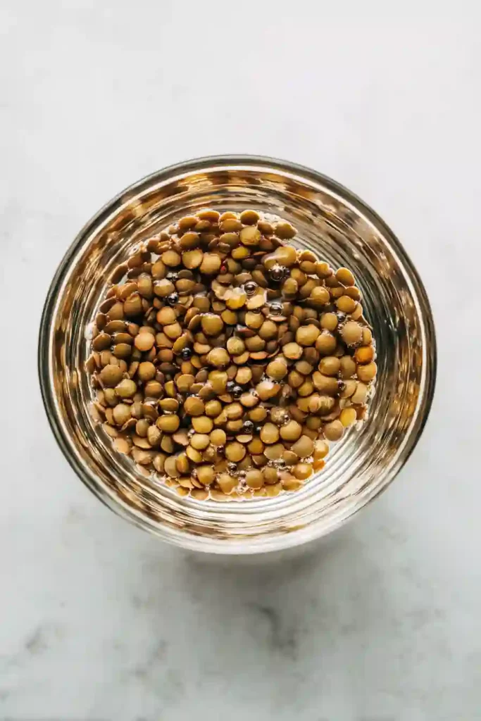 dried lentils being rinsed in glass bowl with water on marble countertop