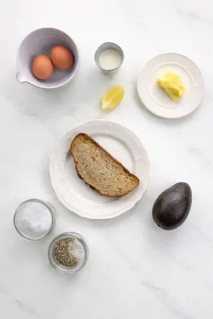 Scrambled Eggs with Avocado Toast 3 Overhead layout of ingredients for scrambled eggs with avocado including eggs, butter, cream, lemon, bread, avocado, salt and pepper