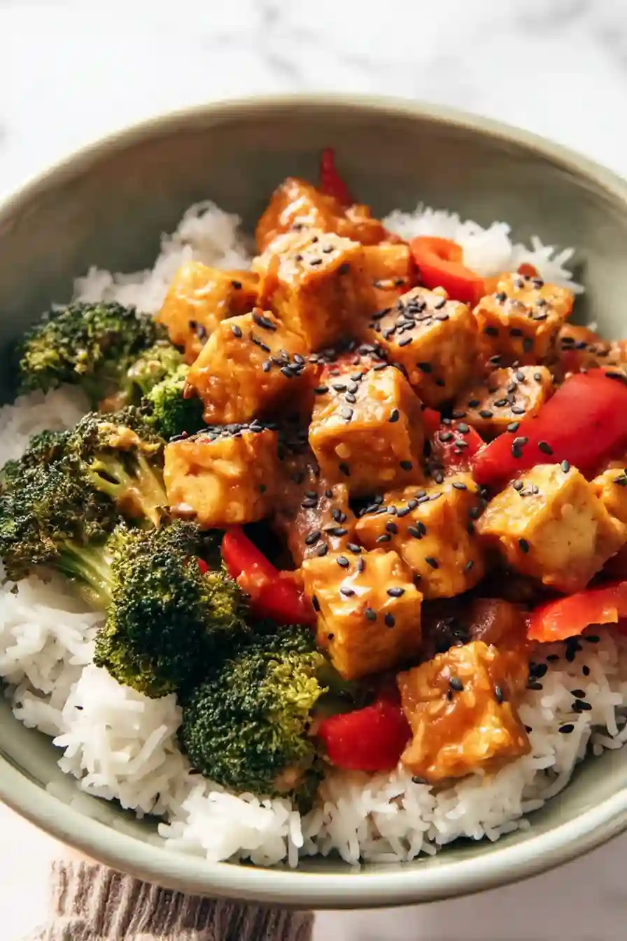Close-up peanut tofu rice bowl with broccoli and peppers in green bowl