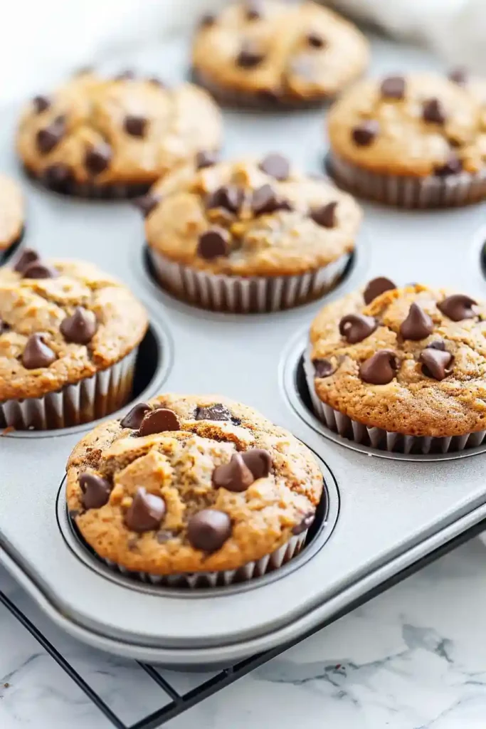Healthy Banana Protein Muffins (Moist, Fluffy & High-Protein!) 4 Freshly baked healthy banana protein muffins cooling in muffin pan on marble countertop