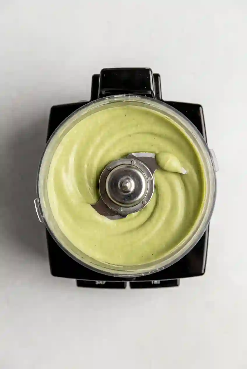 Top view of creamy green avocado sauce blended smooth inside a food processor