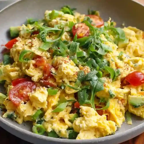 Creamy veggie scrambled eggs with avocado, cherry tomatoes, spinach, and green onions in a skillet