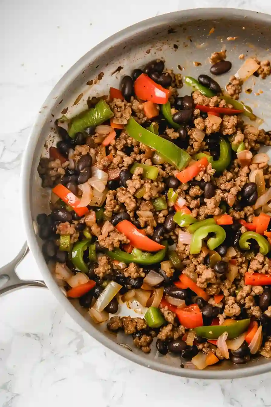 Lean ground beef browning in a skillet with peppers, onions, and black beans
