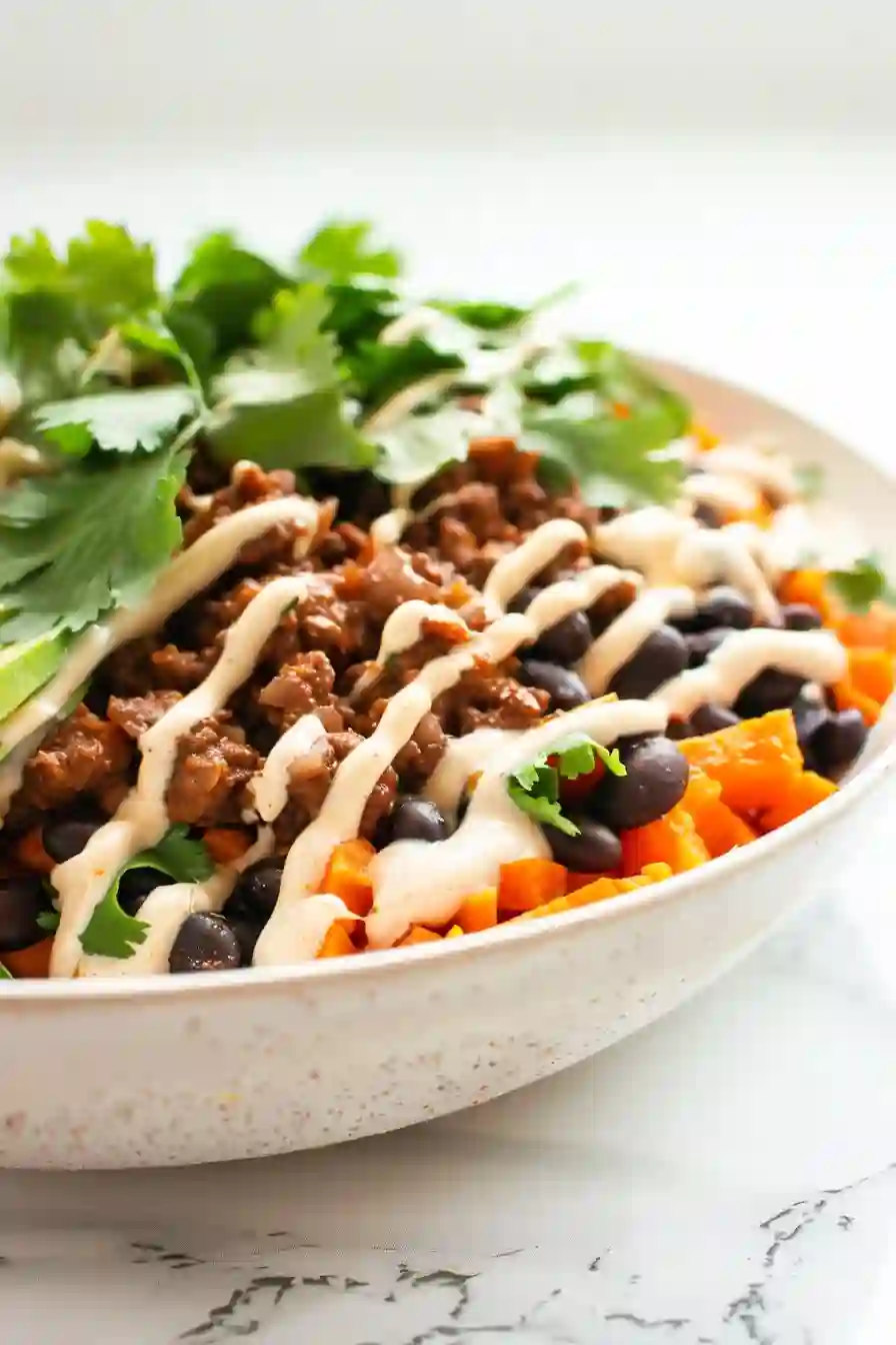 Building the High Protein Taco Bowl Assembled high protein taco bowl with roasted sweet potatoes, cheesy taco beef mixture, black beans, and chipotle crema