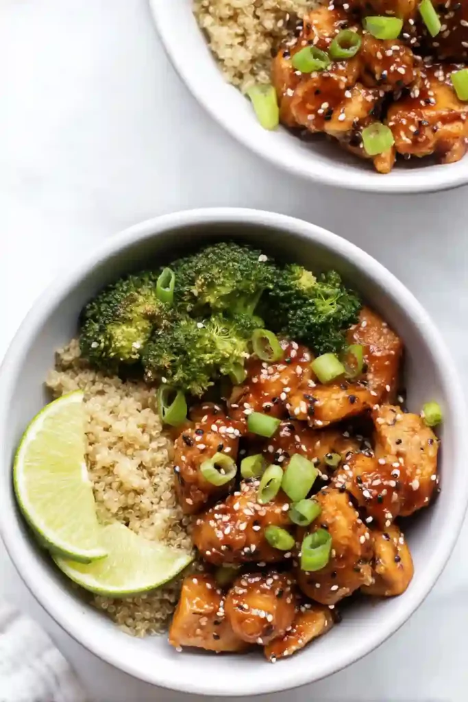 Meal Prep Honey Garlic Chicken Bowls 12 Completed honey garlic chicken meal prep bowl garnished with sesame seeds, green onions, and lime wedges.