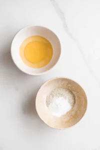 Meal Prep Honey Garlic Chicken Bowls 4 Two small bowls on a white marble countertop, one filled with beaten egg and the other with seasoned cornstarch for coating chicken.