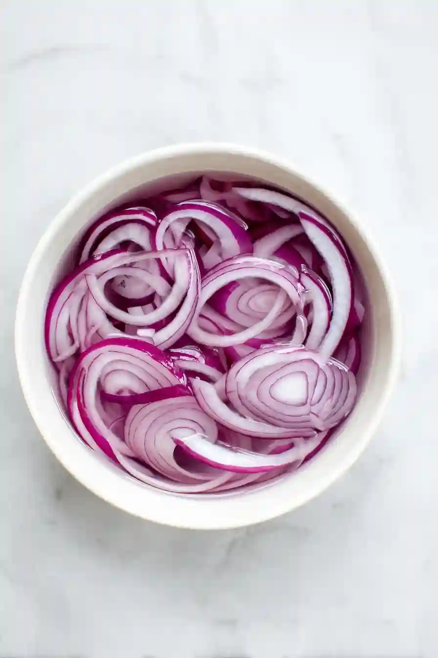 Thinly sliced red onion soaking in cold water inside a small bowl before adding to salad.