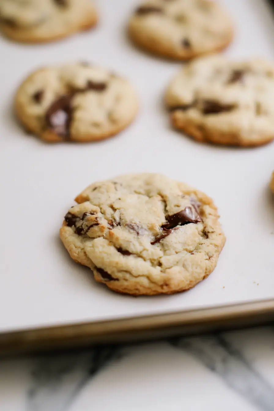 Freshly baked almond flour chocolate chip cookies cooling on a baking sheet with golden edges and melted chocolate chips.