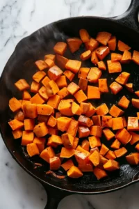 Healthy Ground Beef and Zucchini Skillet 4 Diced sweet potatoes sautéing in avocado oil in a black cast iron skillet on a white marble countertop.
